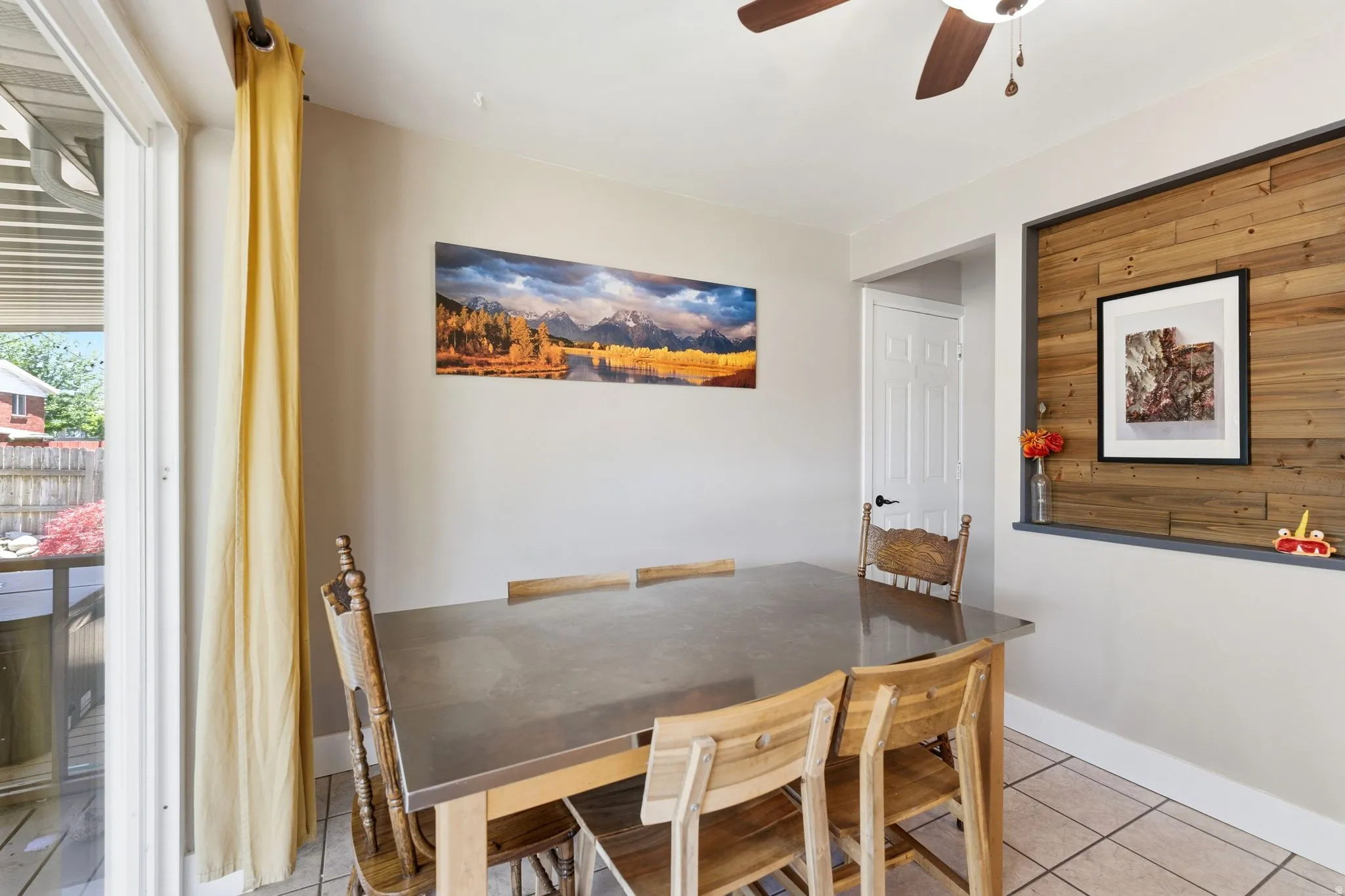 Dining area featuring tile flooring, a wood-paneled accent wall, and a ceiling fan