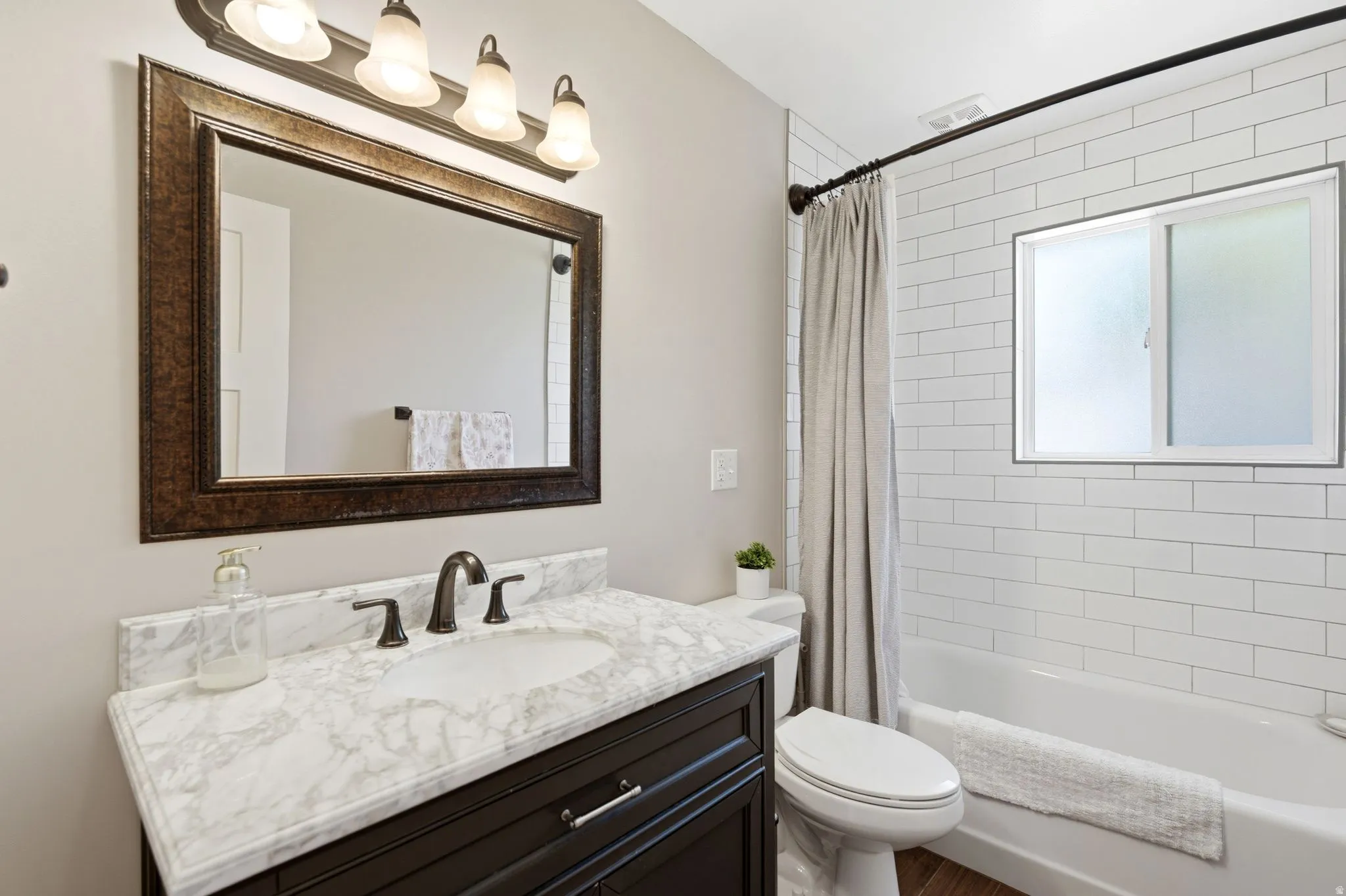 Bathroom featuring a dark wood vanity with a white marble-patterned countertop, a decorative framed mirror, and a four-bulb vanity light fixture