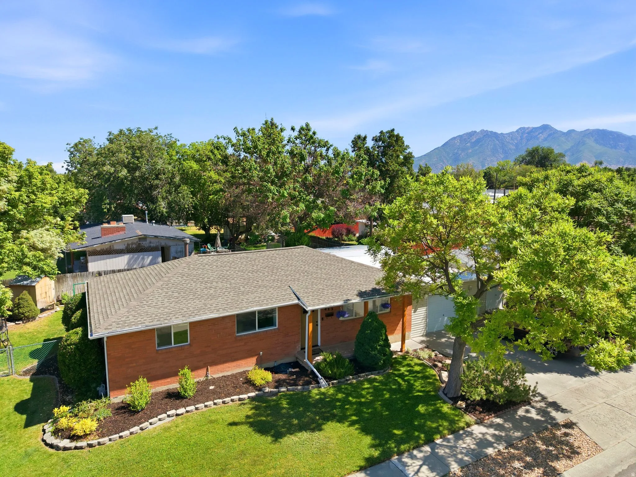 Brick facade residence with a gabled roof, mature trees, landscaped front yard, and mountain backdrop