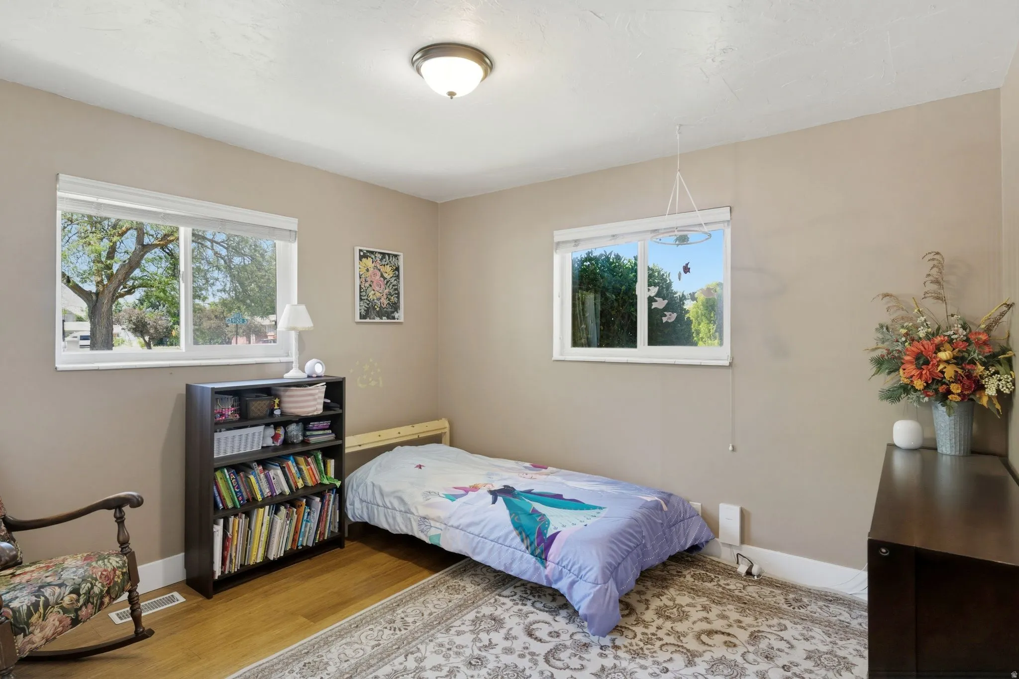 Bright room featuring two windows with roller shades, wood-finish flooring, and light neutral wall tones