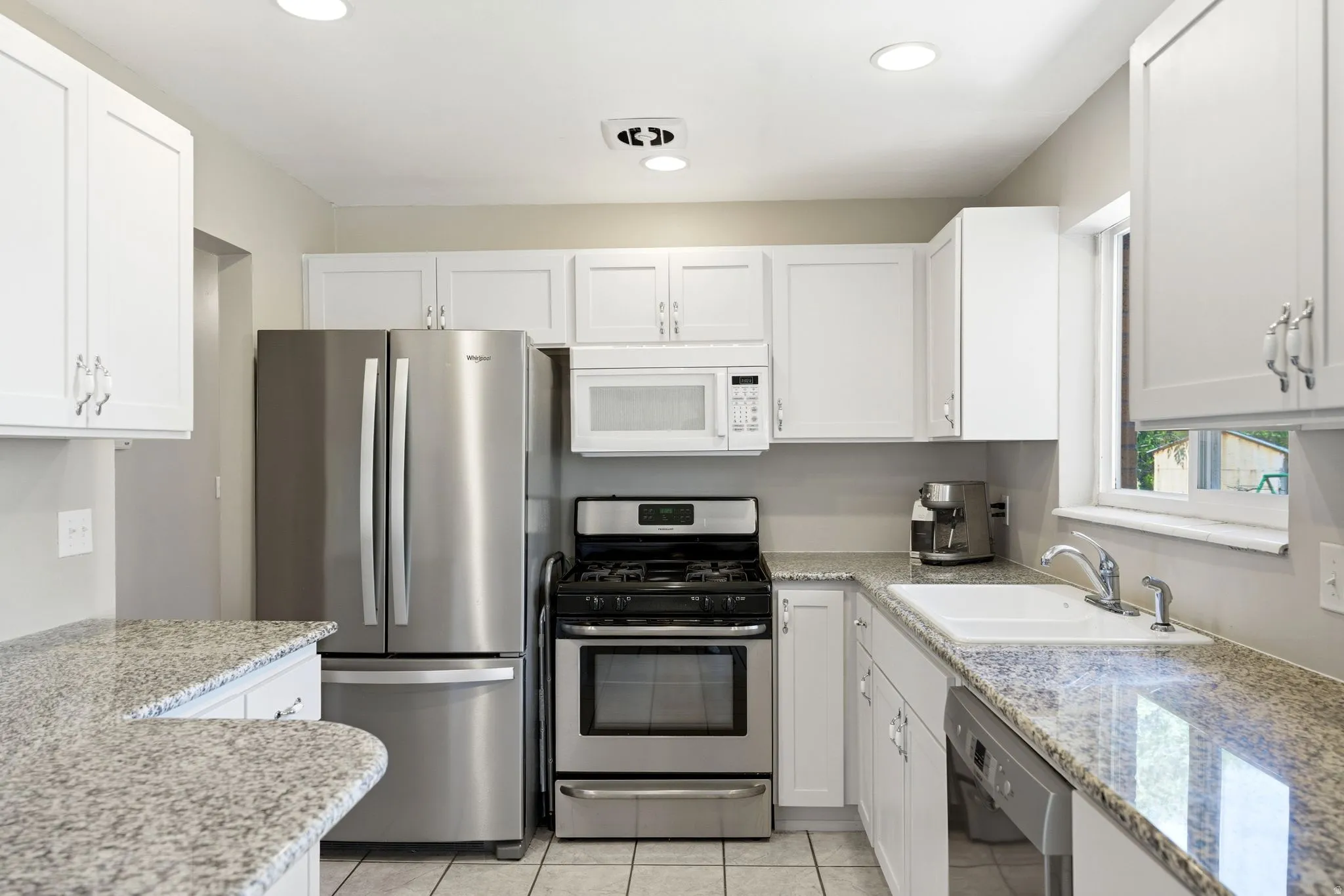 Kitchen featuring white shaker-style cabinetry, granite countertops, and stainless steel appliances including a refrigerator, range, microwave, and dishwasher