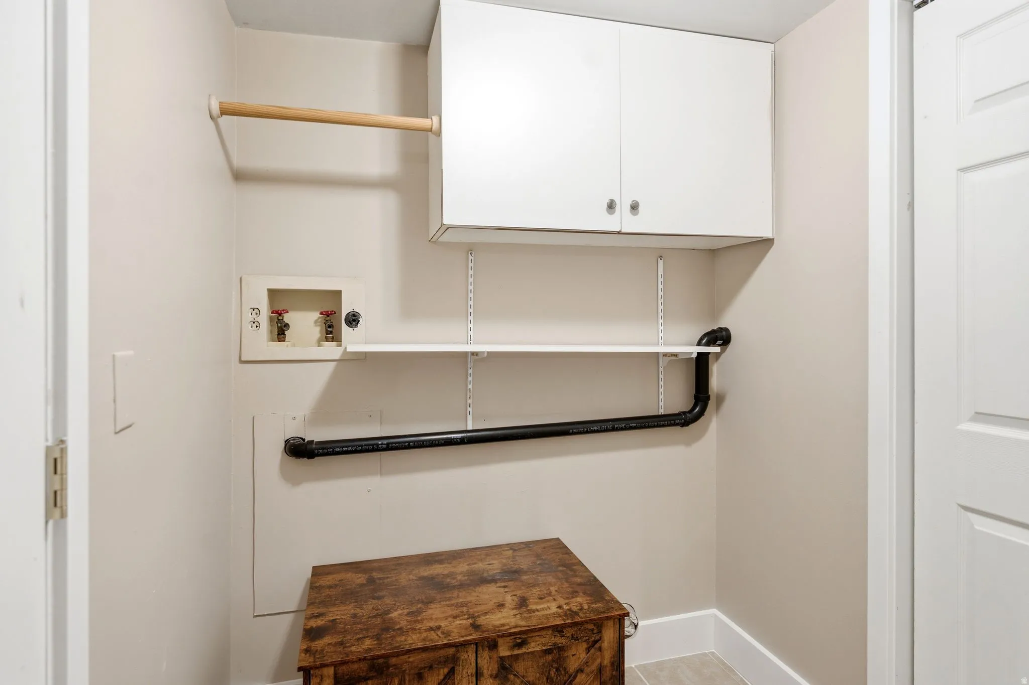 Dedicated laundry area featuring white upper cabinetry, a wooden hanging rod, adjustable white shelving, and essential plumbing connections