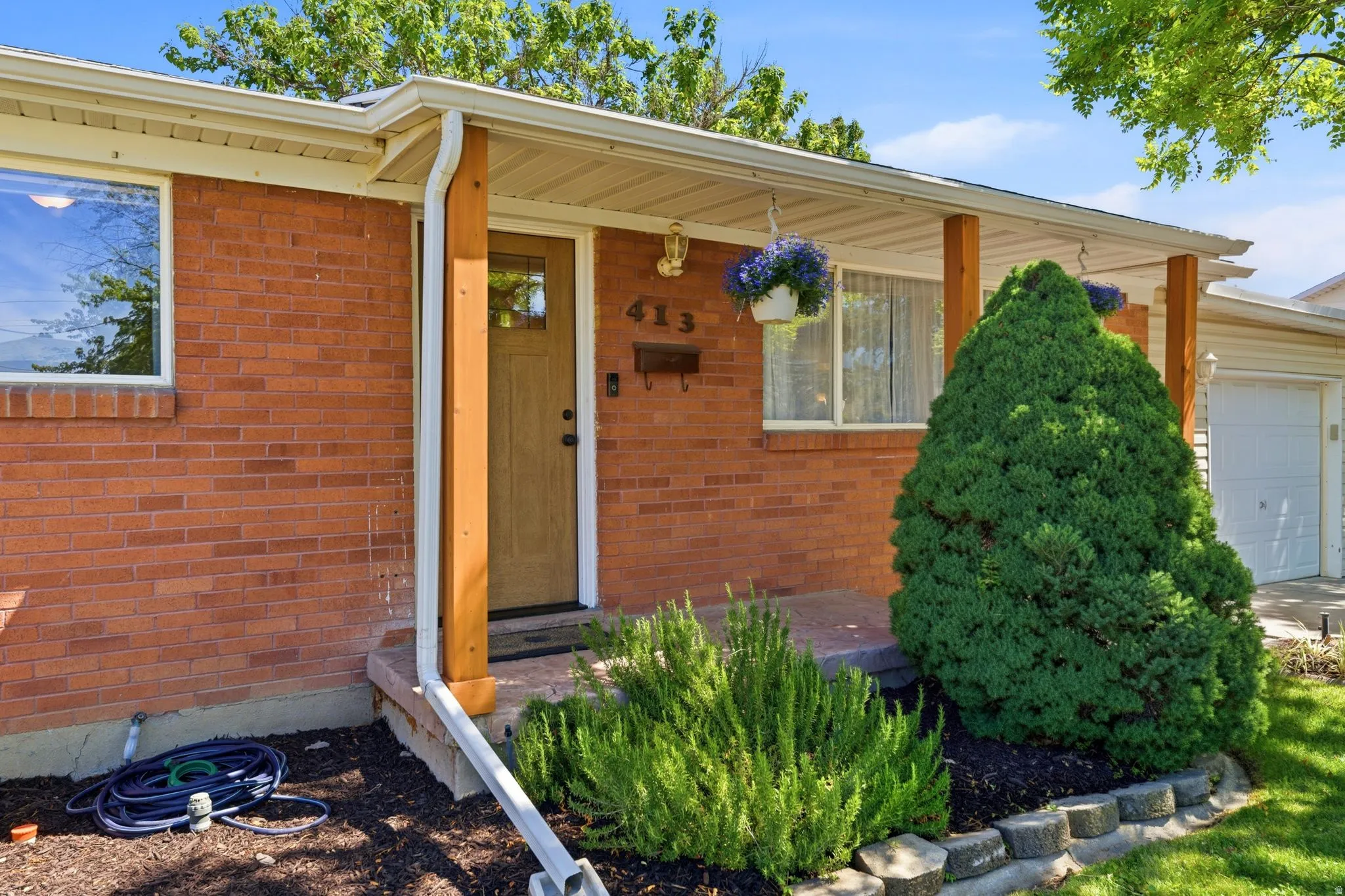 Brick exterior with a covered porch entry, featuring a wood-tone front door, white-framed windows, and a detached garage
