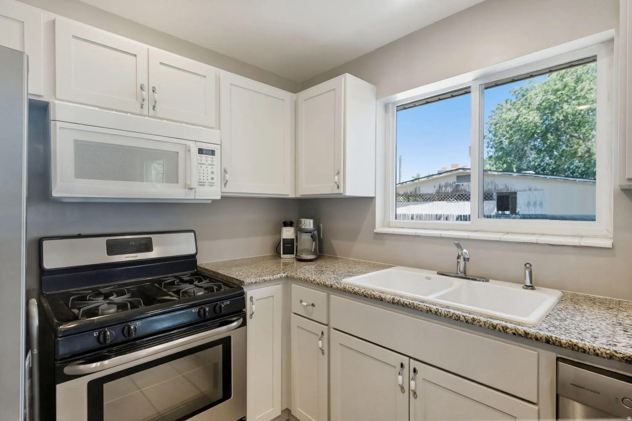 Kitchen featuring white shaker-style cabinetry, granite-finish countertops, stainless steel appliances, a double basin sink, and a large window