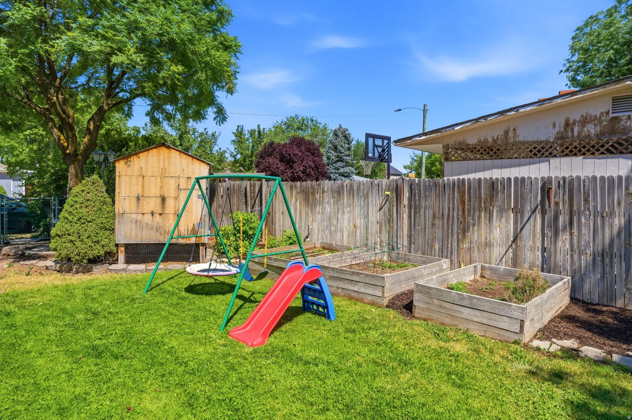 Expansive backyard featuring a lush green lawn, mature trees, a wooden privacy fence, and multiple raised garden beds