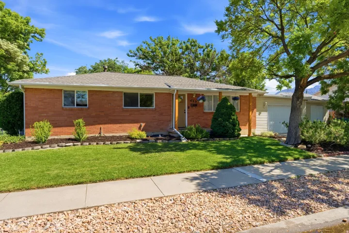 Brick-front ranch-style residence featuring a lush green lawn and mature trees
