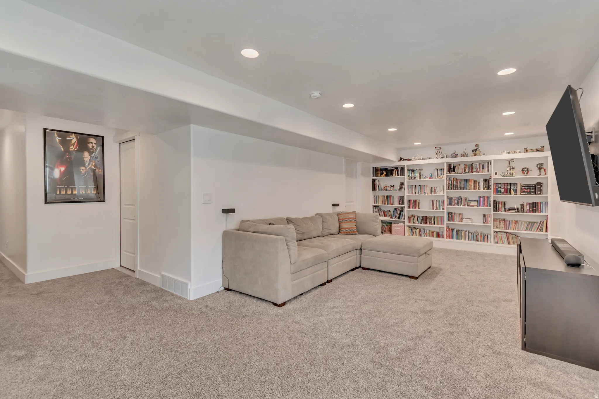 Spacious room featuring light gray carpet, recessed lighting, white walls, and extensive built-in shelving