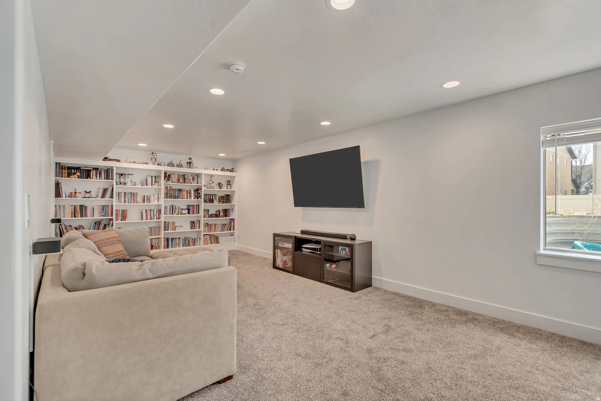 Spacious room featuring extensive built-in shelving, recessed lighting, a window with blinds, and soft carpet flooring