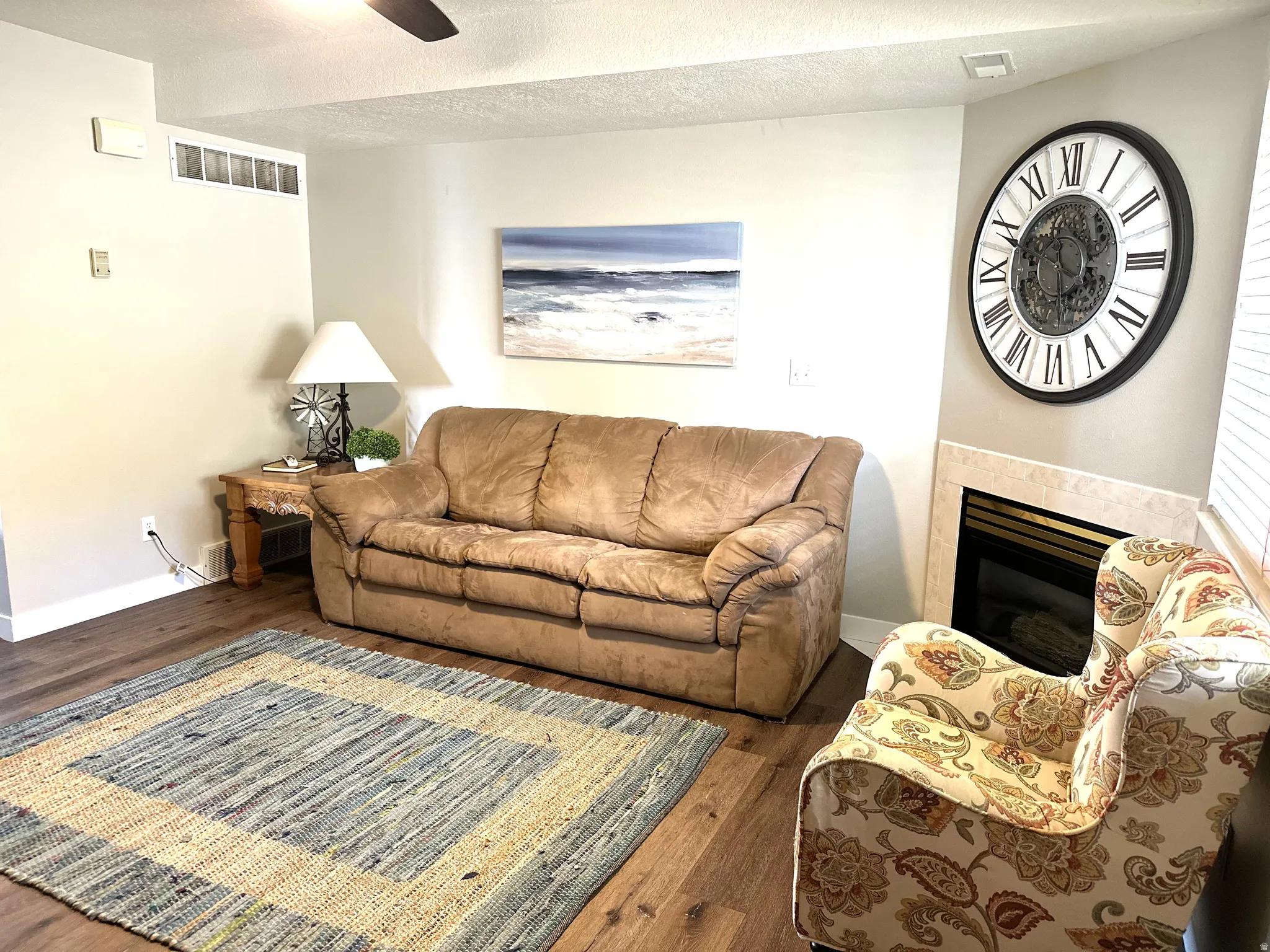 Living area featuring wood-finish flooring, a corner fireplace with a tiled surround, and a ceiling fan
