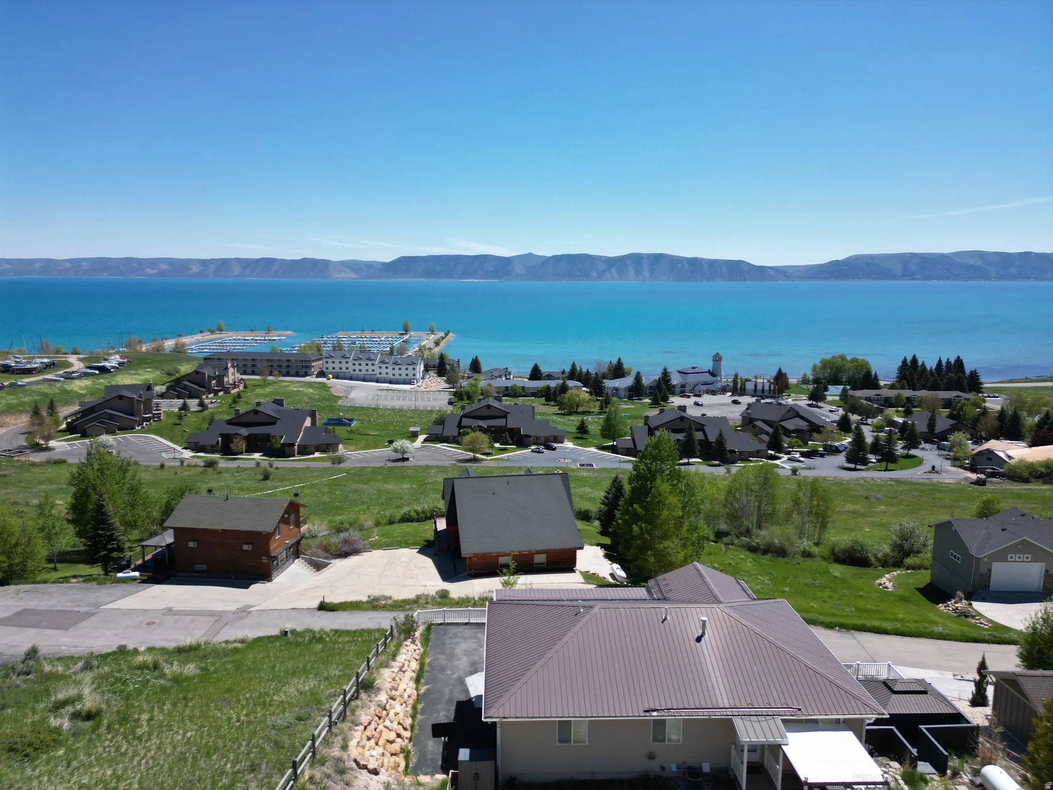 Expansive aerial view showcasing a large body of water with distant mountains, a marina, and multiple structures