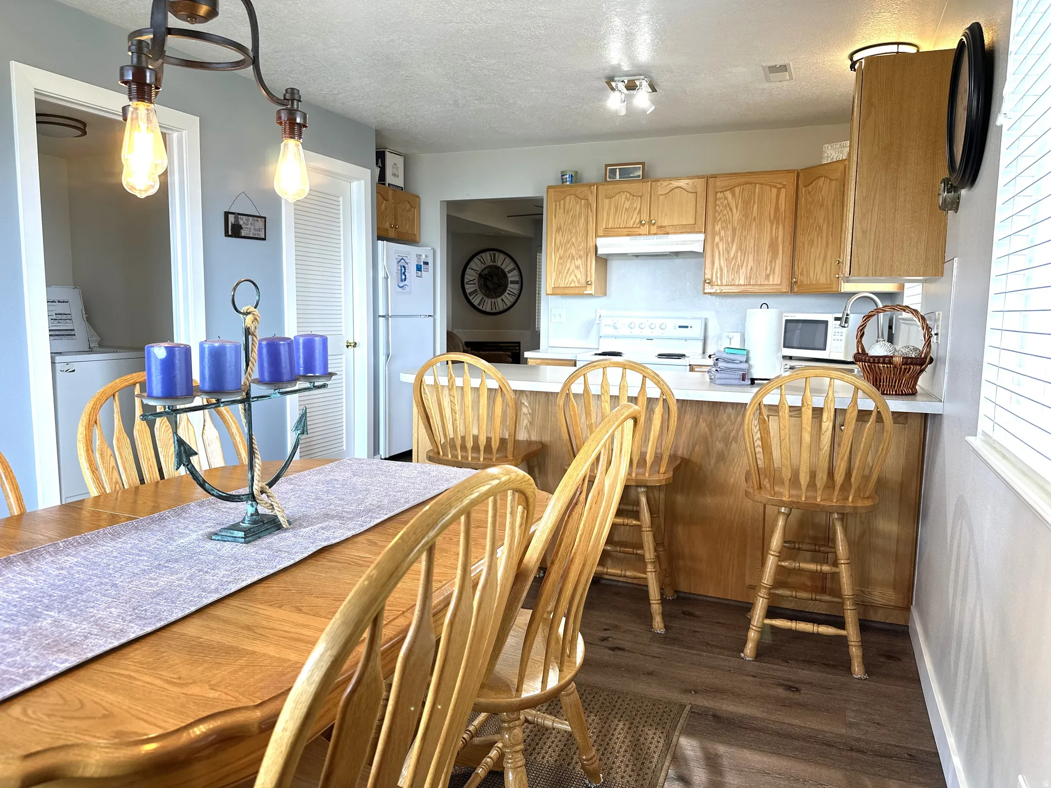 Kitchen and dining area featuring wood-finish flooring, light wood cabinetry, white countertops, and a breakfast bar with seating