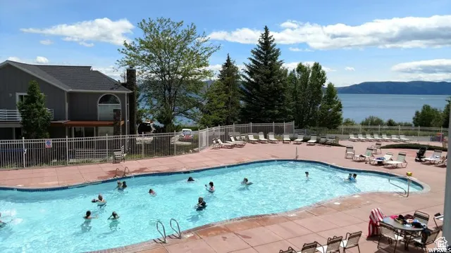 Expansive outdoor swimming pool with surrounding concrete decking, lounge chairs, and a white metal fence