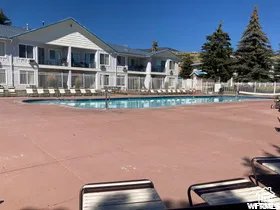 Expansive outdoor swimming pool area featuring a blue-tiled pool, a concrete pool deck, and perimeter fencing