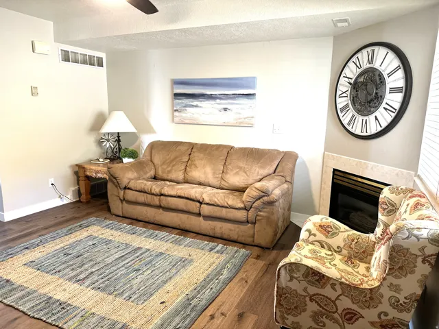 Living area featuring wood-finish flooring, a corner fireplace with a tiled surround, and a ceiling fan