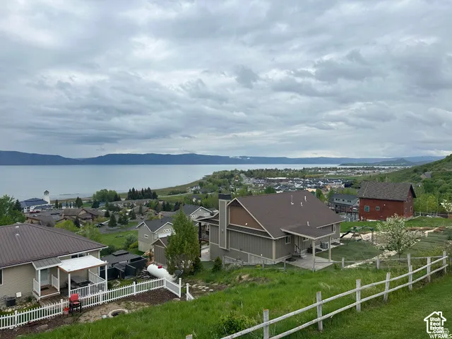 Property featuring a two-story residence with a covered deck, partial white picket fence, and a terraced backyard