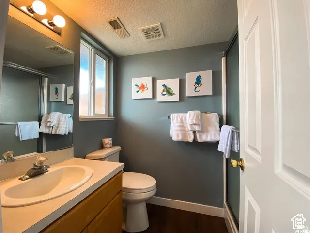 Bathroom featuring a single vanity with a white basin sink, an overhead light bar, a toilet, a privacy window, and dark wood-finish flooring