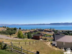 Expansive lake and mountain scenery from a sloped property featuring a rustic split-rail fence