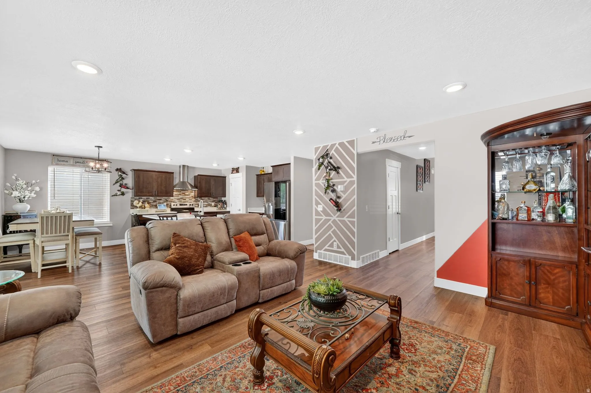 Open-concept living space featuring wood-finish flooring, recessed lighting, and a kitchen with dark cabinetry and stainless steel appliances