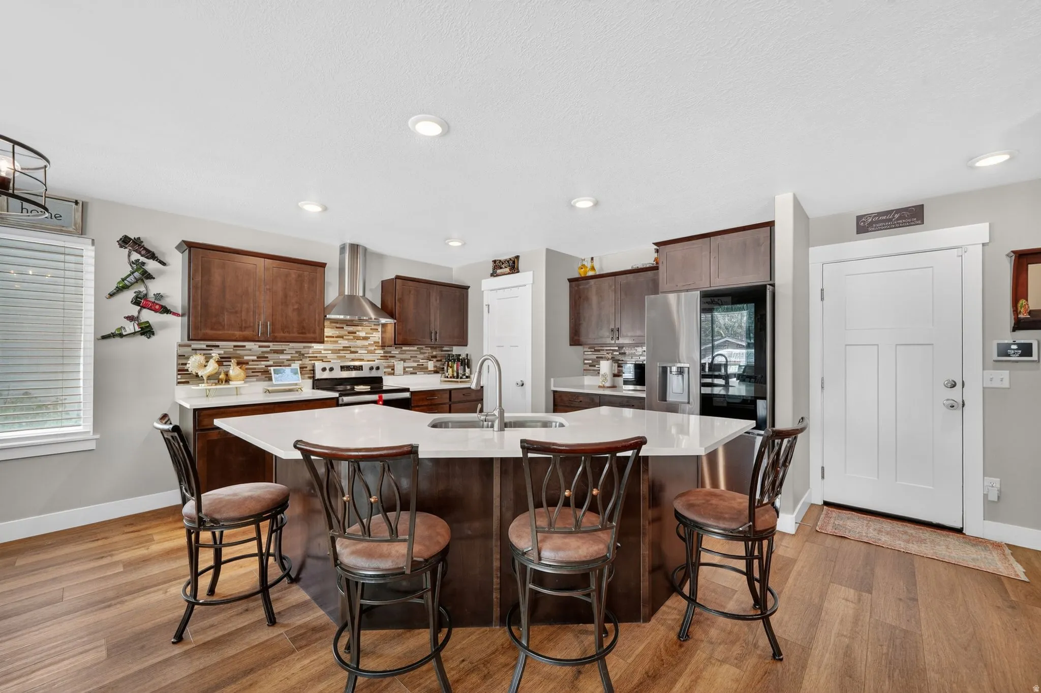 Kitchen featuring a multi-sided island with a white countertop and seating, wood-finish flooring, recessed lighting, stainless steel appliances, and dark wood cabinetry