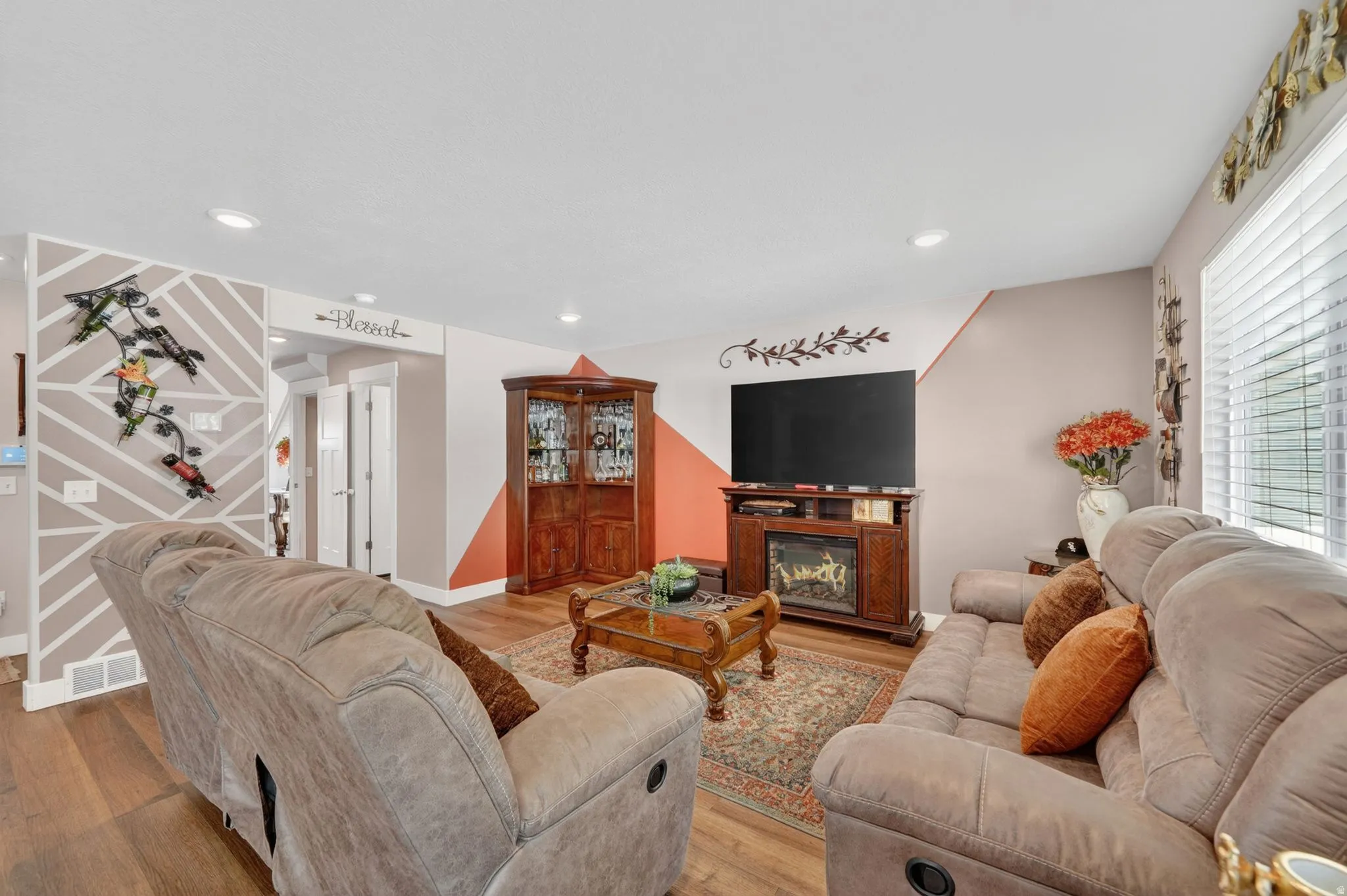 Living area featuring wood-finish flooring, recessed lighting, a corner display cabinet with glass doors, and a built-in electric fireplace entertainment center