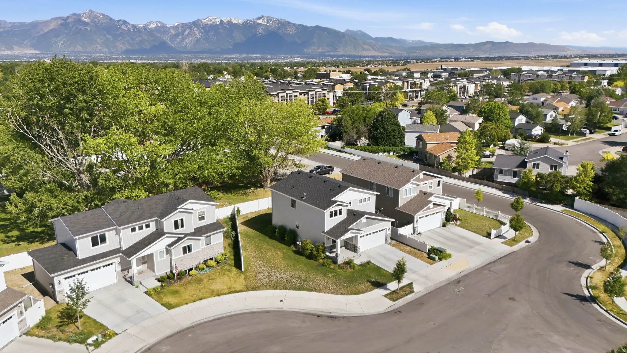 Modern residential development featuring a curved streetscape, mature trees, and mountainous terrain in the background