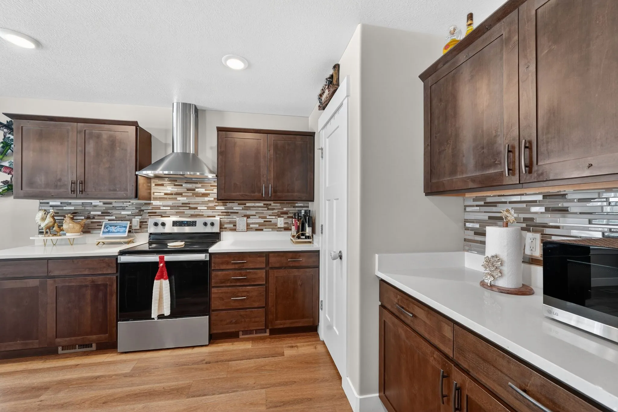 Kitchen featuring wood-finish flooring, dark wood cabinetry, light countertops, and a full-height tile backsplash