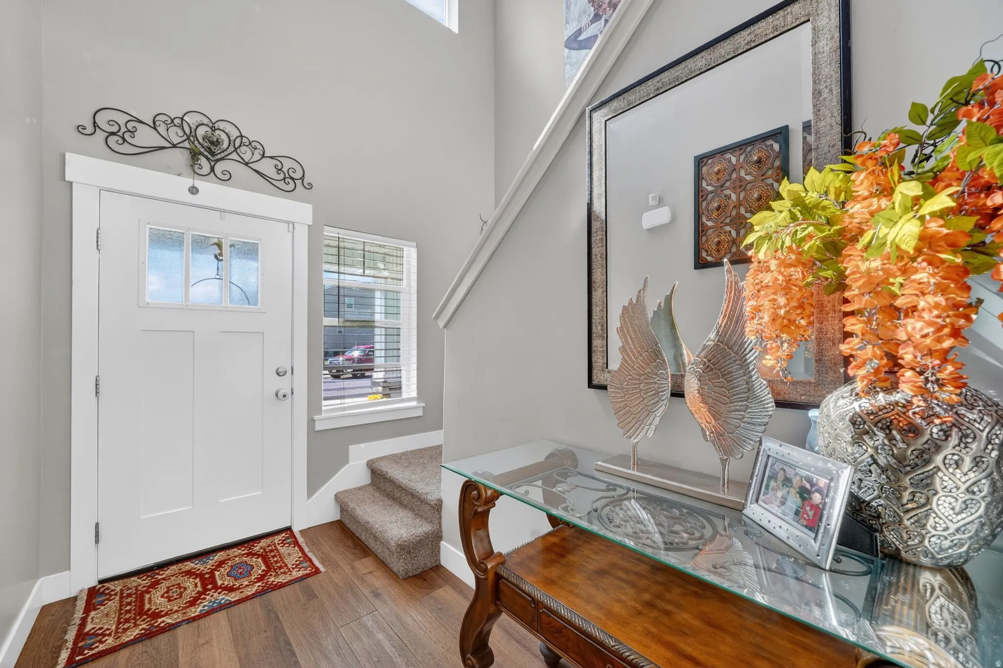 Entryway featuring wood-finish flooring, a white paneled door with glass inserts, a side window with blinds, and a carpeted staircase