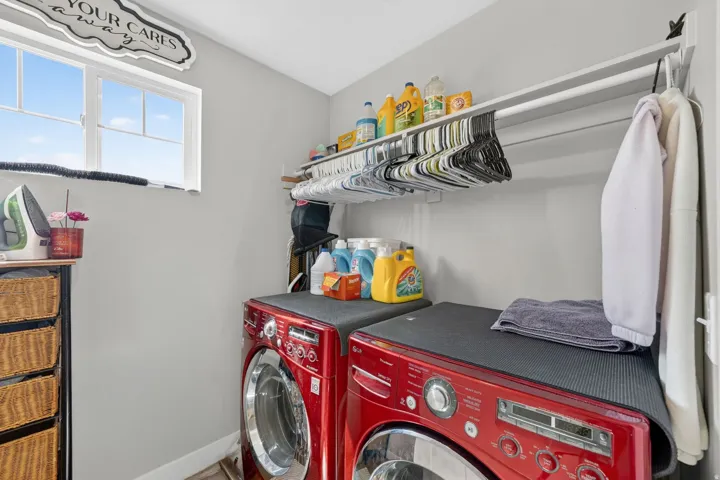 Dedicated laundry space featuring a window, built-in shelving, a clothes hanging rod, and two red front-loading appliances