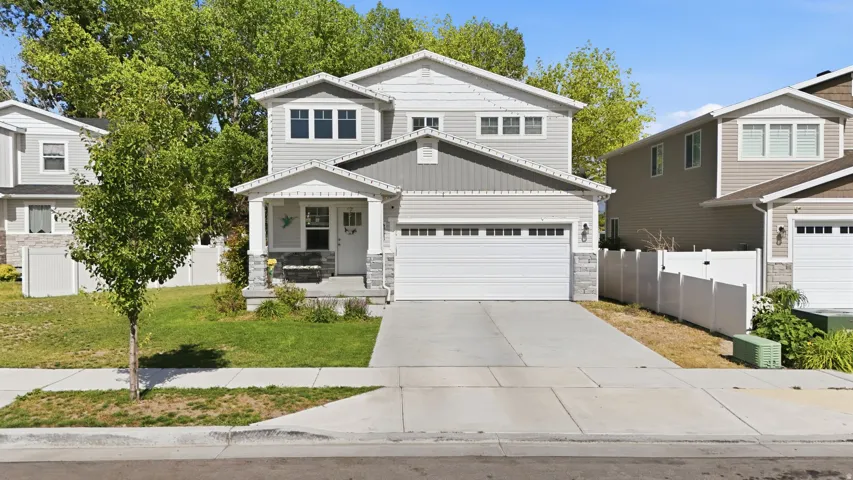 Two-story residence featuring light gray siding with dark gray accent shingles, a covered front porch, and a two-car garage