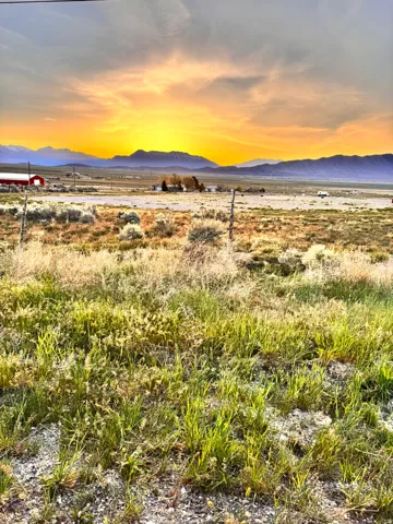 Expansive natural landscape featuring varied vegetation, distant mountain ranges, and a prominent sunset in the background