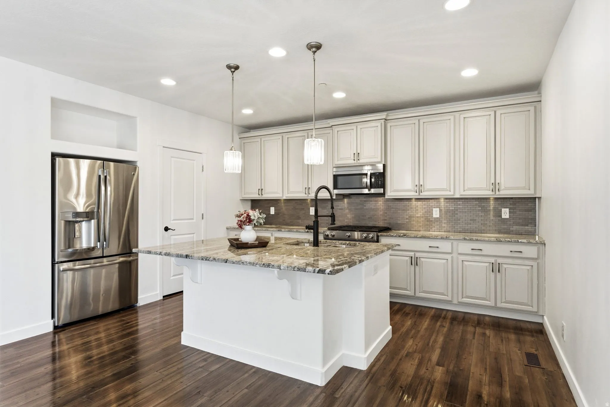 Kitchen featuring a central island with a multi-toned countertop, stainless steel appliances, white cabinetry with dark hardware, a mosaic tile backsplash, and wood-finish flooring