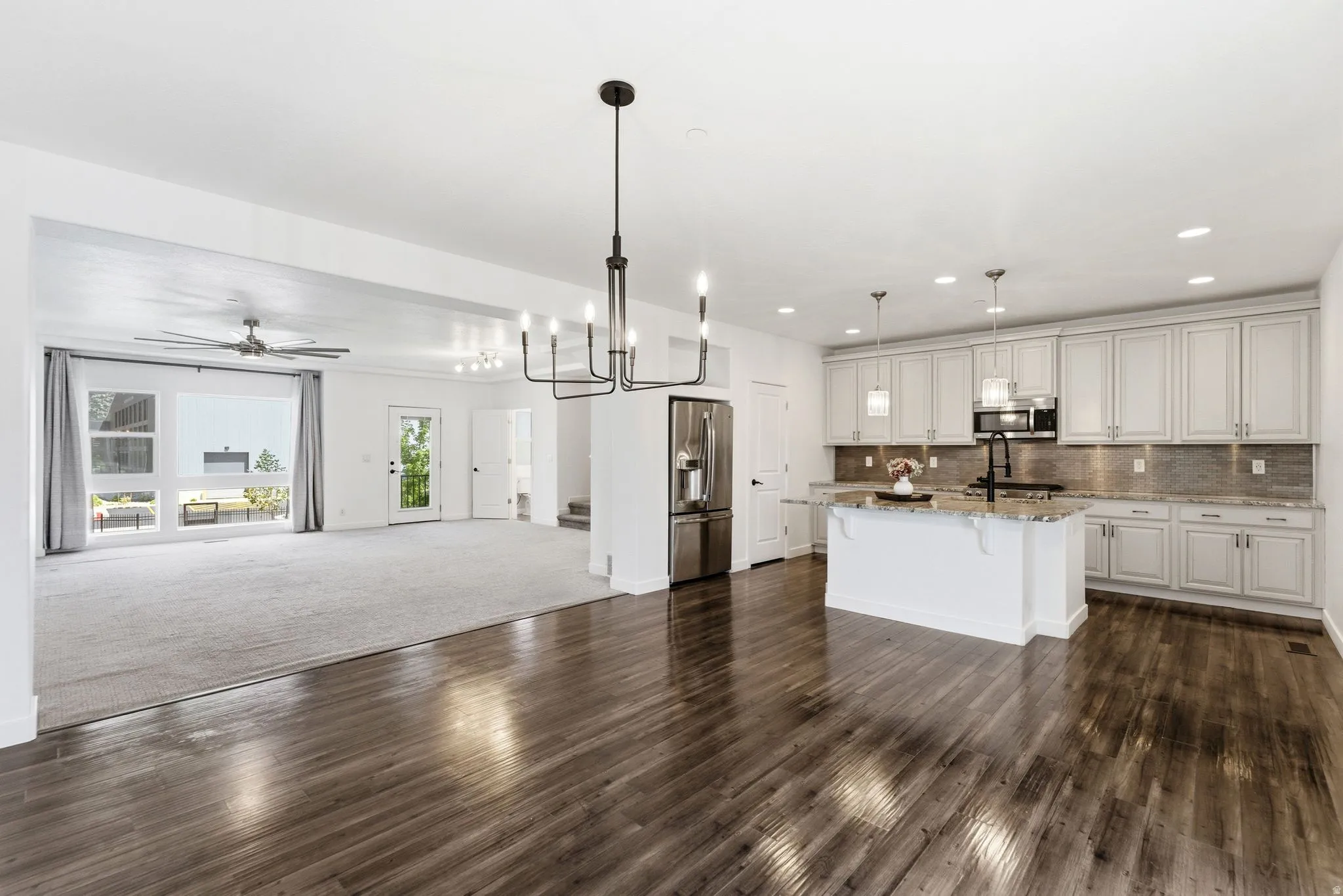 Open-concept living space featuring wood-finish flooring, a contemporary kitchen, and an expansive carpeted area