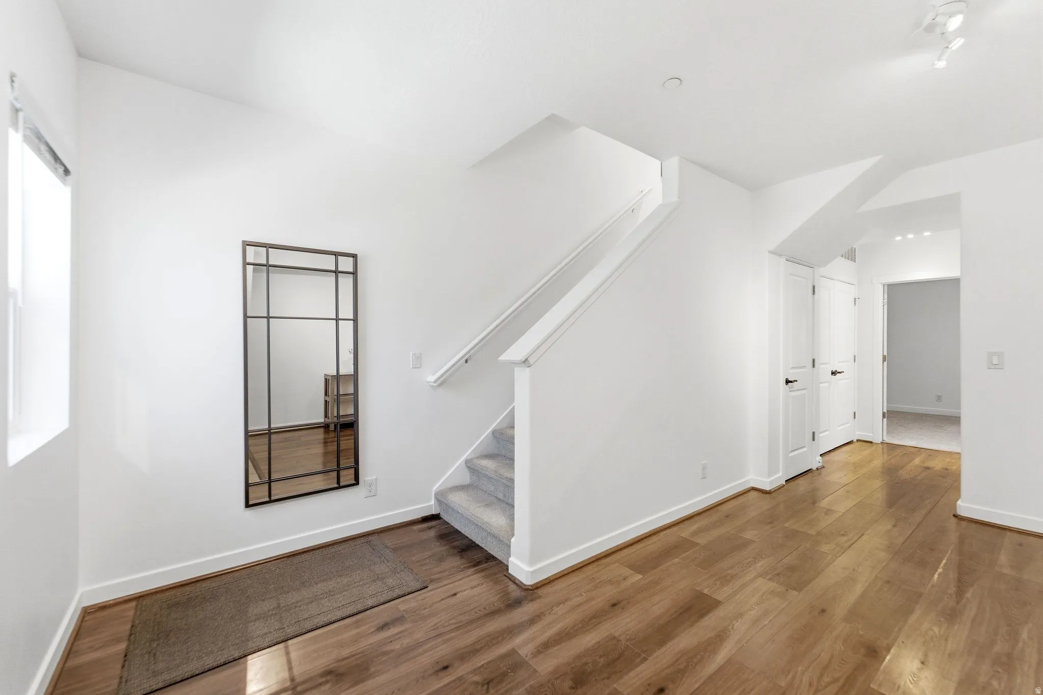 Entryway featuring wood-finish flooring, white walls, and a carpeted staircase with a white handrail