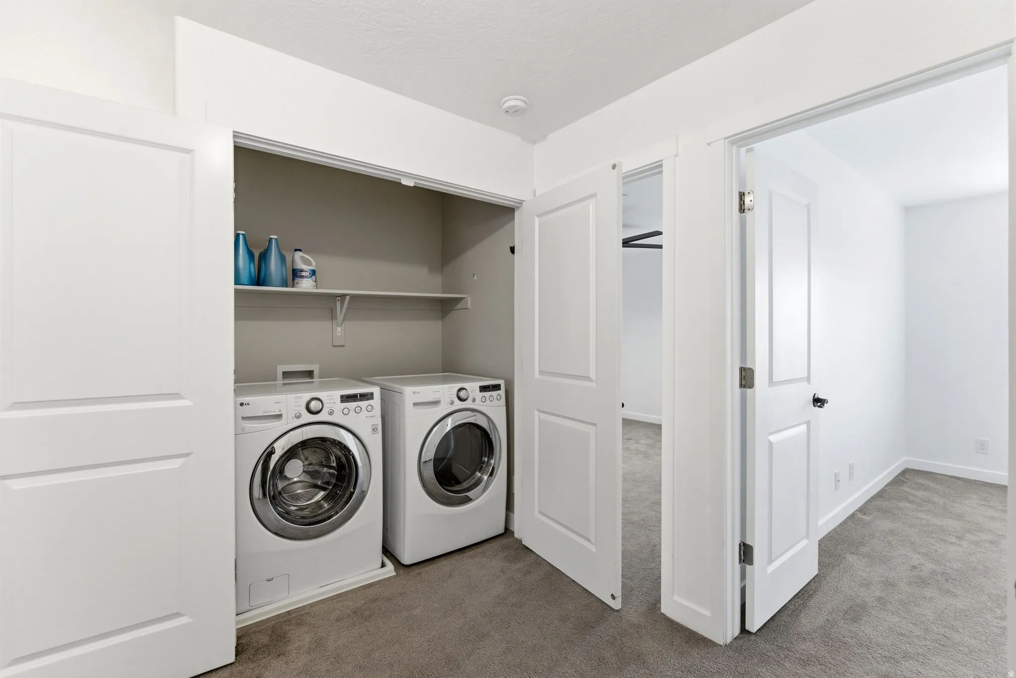 Dedicated laundry closet with front-loading washer and dryer, featuring overhead shelving