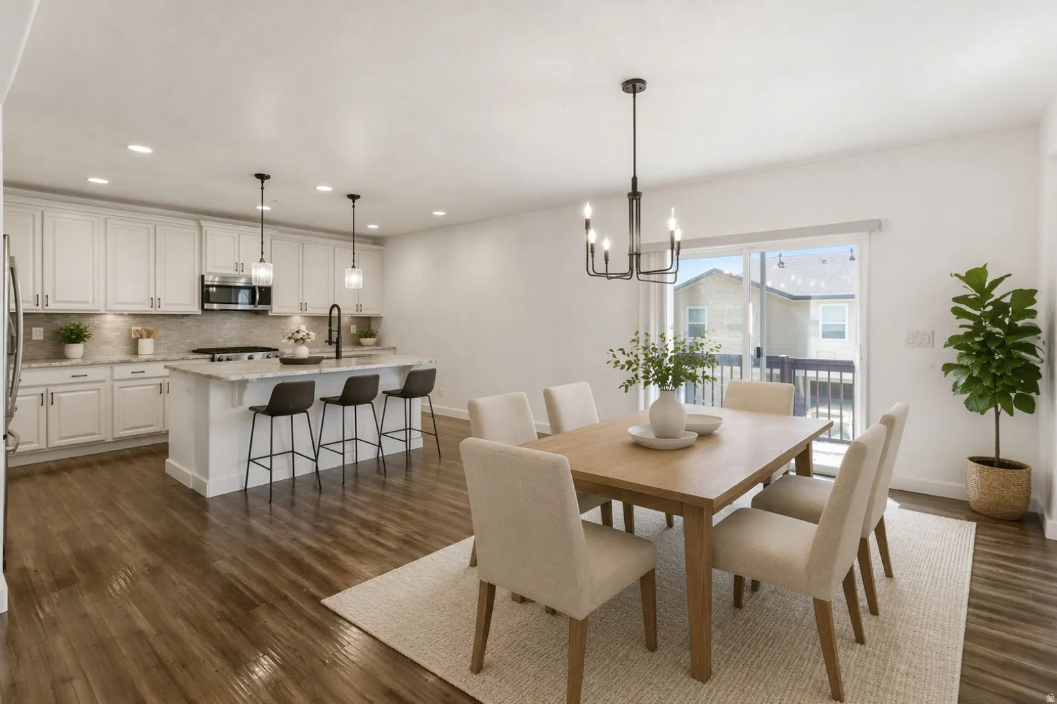 Open-concept living space with wood-finish flooring, a contemporary dining area, and a kitchen featuring white cabinetry, an island with seating, and stainless steel appliances