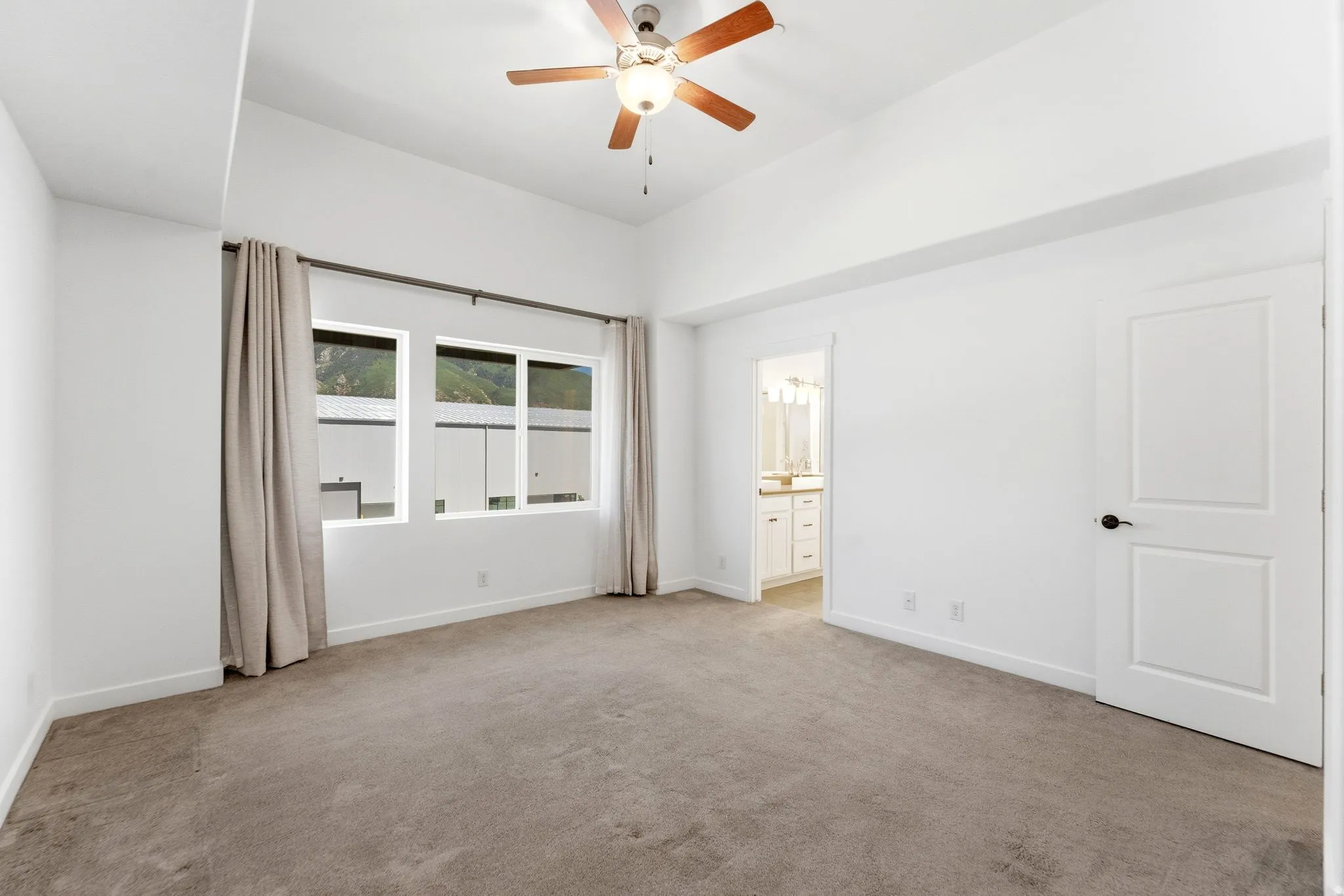 Spacious room featuring vaulted ceilings, a wood-finish ceiling fan, and large windows with opaque drapery