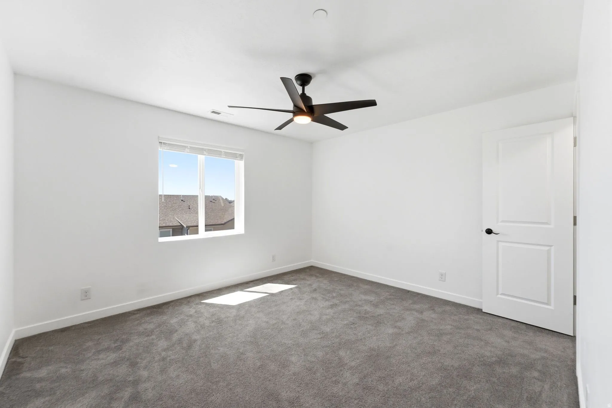Room featuring a white ceiling and walls, gray carpet, and a modern black ceiling fan