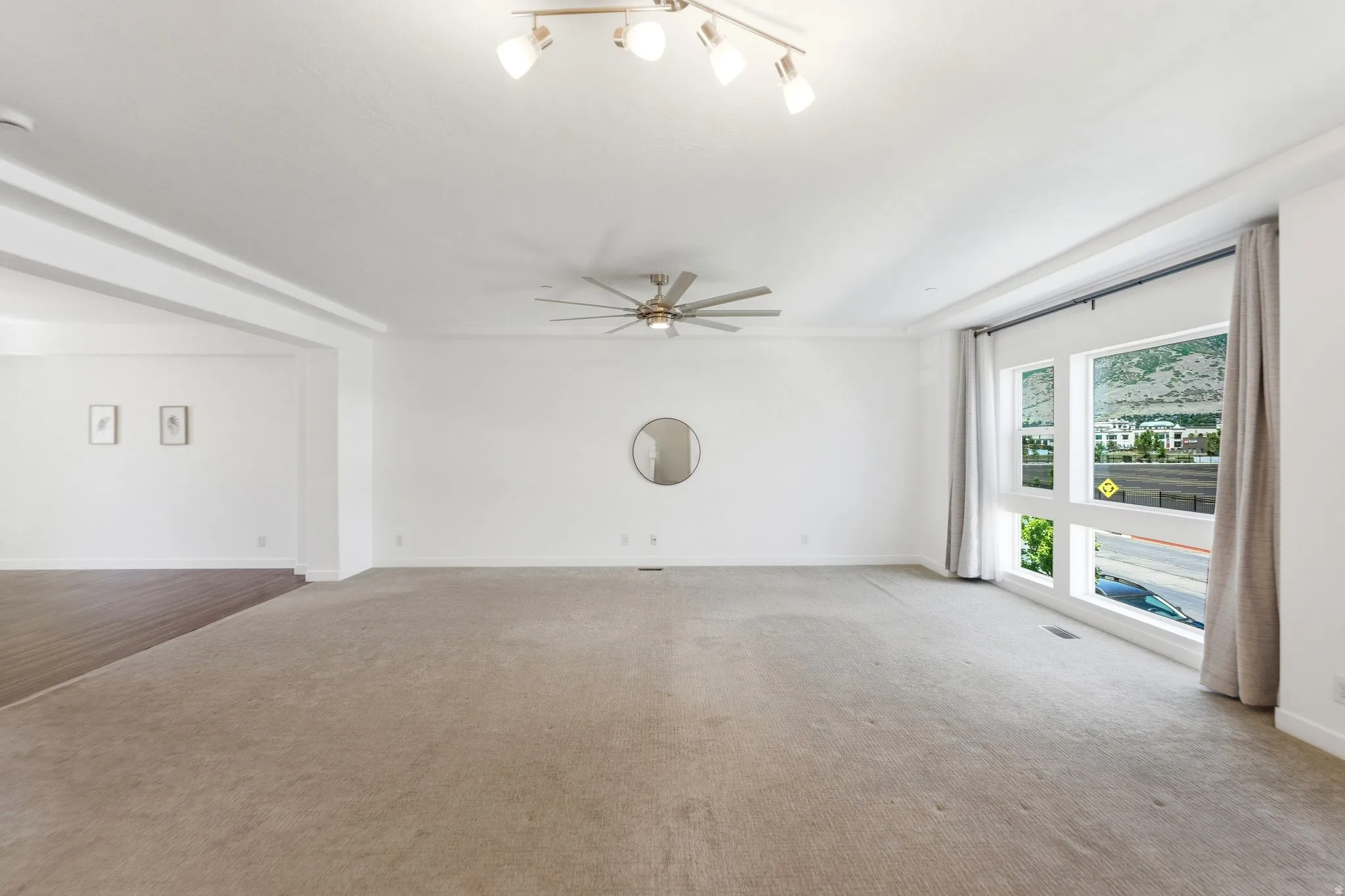 Spacious living area featuring carpet flooring, large windows, recessed ceiling details, a ceiling fan, and track lighting