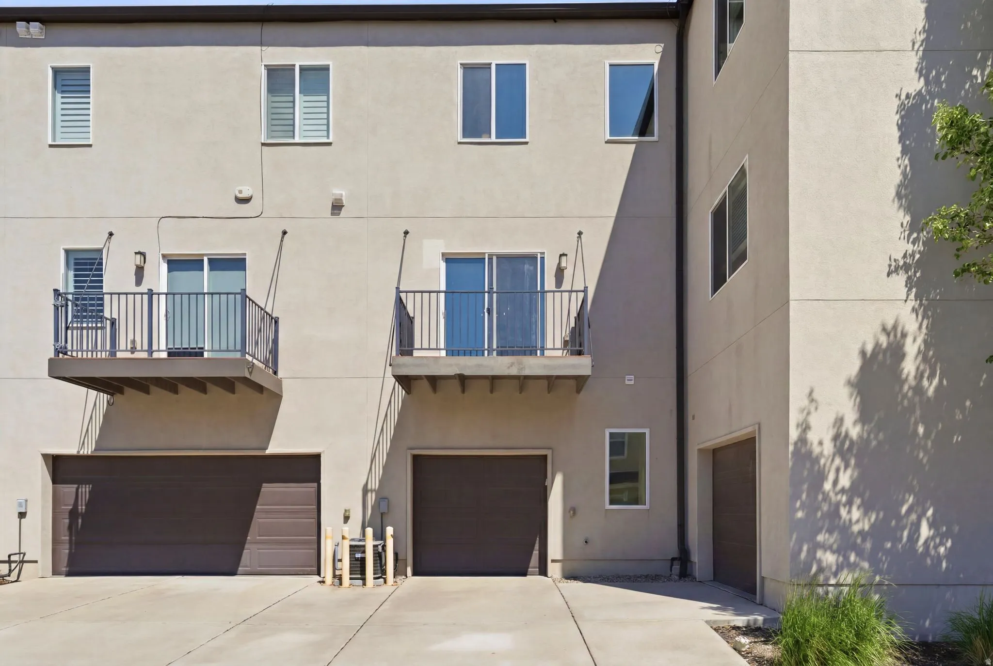 Multi-story stucco exterior featuring two private balconies with metal railings, dual garage doors, and multiple windows with white frames