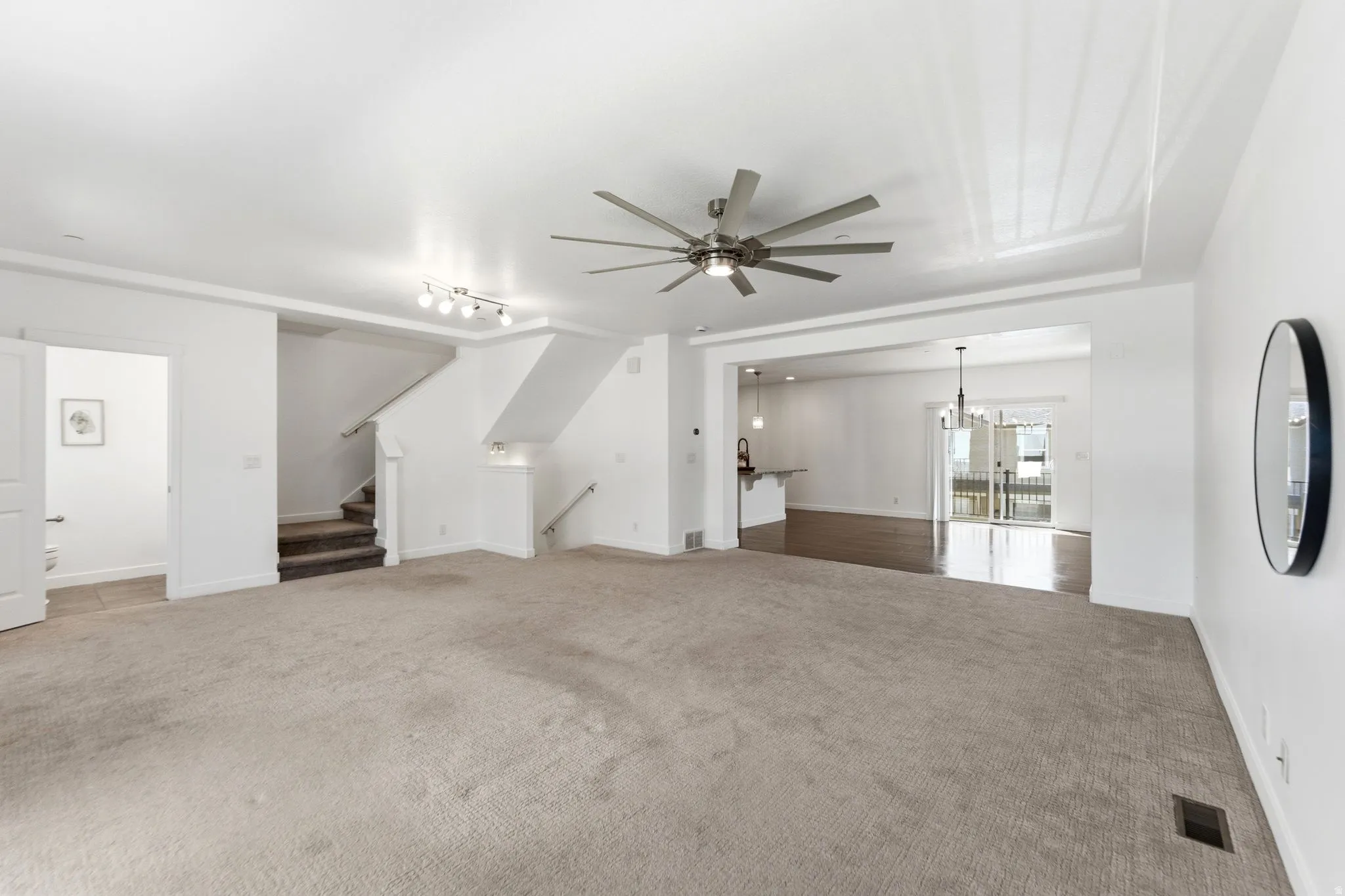 Spacious living area featuring neutral carpeting, a modern ceiling fan, and recessed lighting