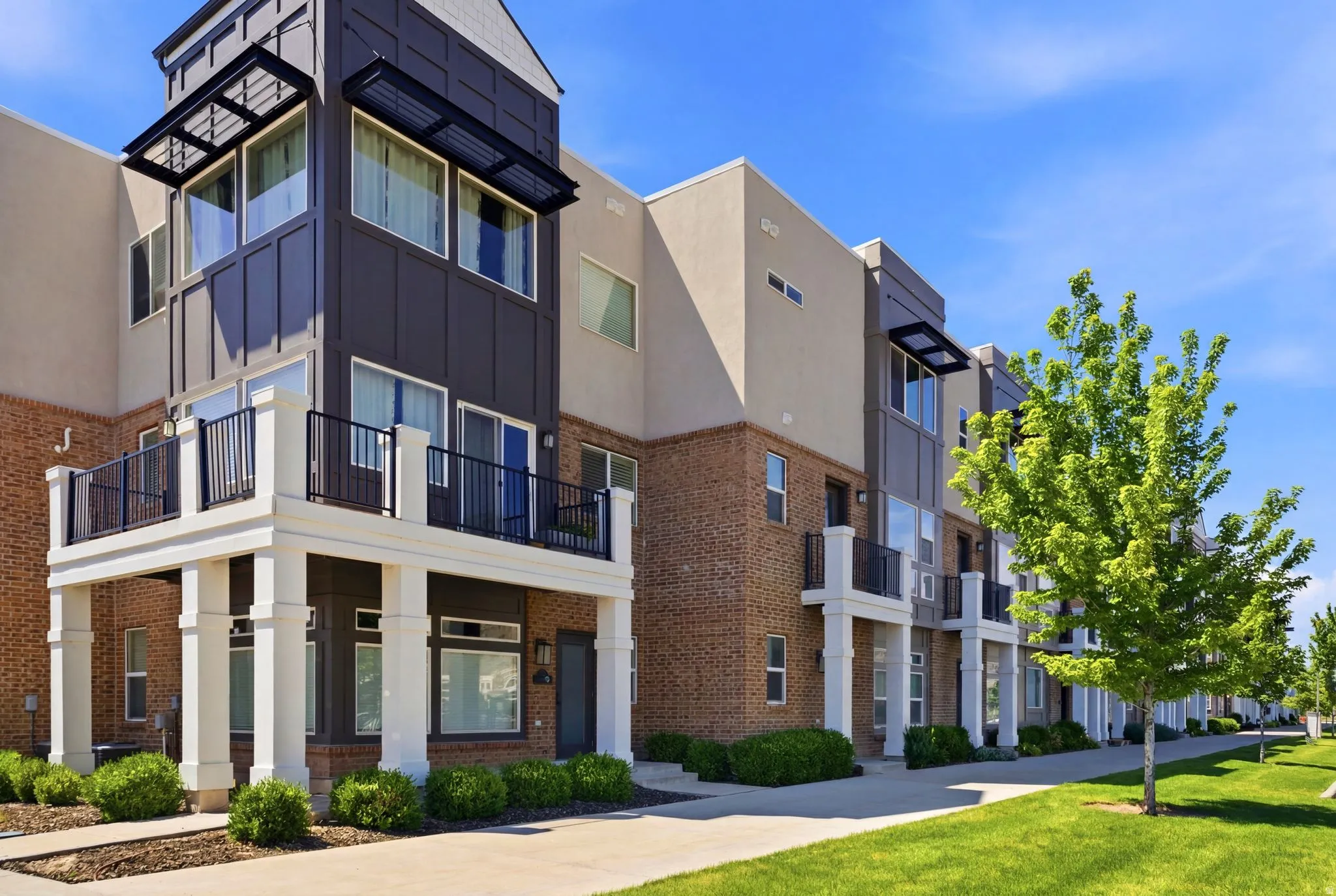 Modern multi-story facade featuring brick and paneling, multiple balconies with black railings, and large windows with sunshades