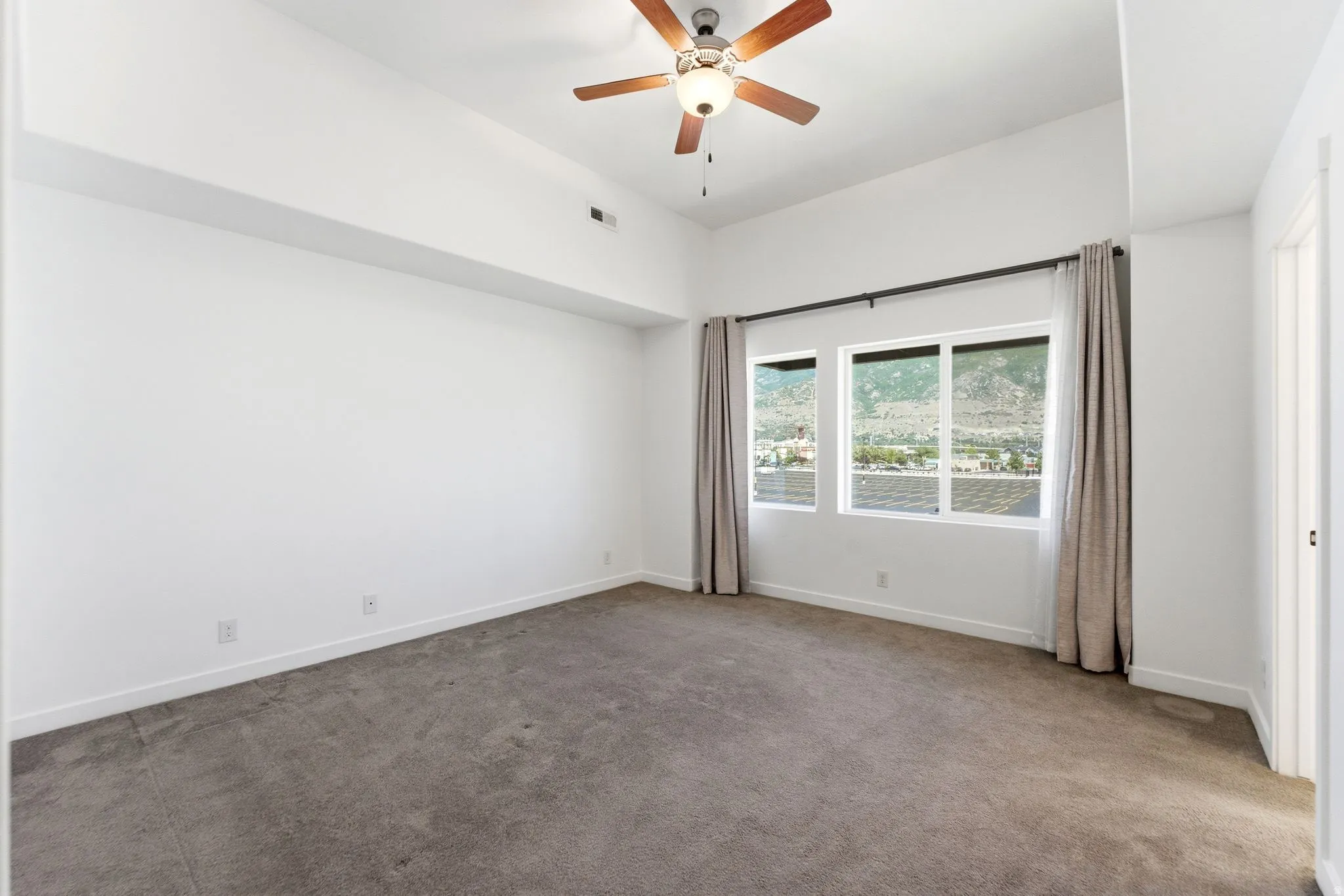 Spacious room with plush carpet flooring, a large window offering a mountain backdrop, a ceiling fan, and high ceilings