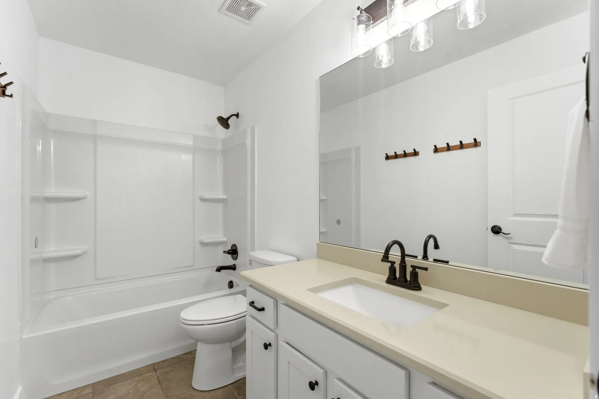 Full bathroom featuring a white tub/shower combination with integrated shelving, a white toilet, and a vanity with a light-toned countertop, integrated sink, and dark bronze-finish fixtures