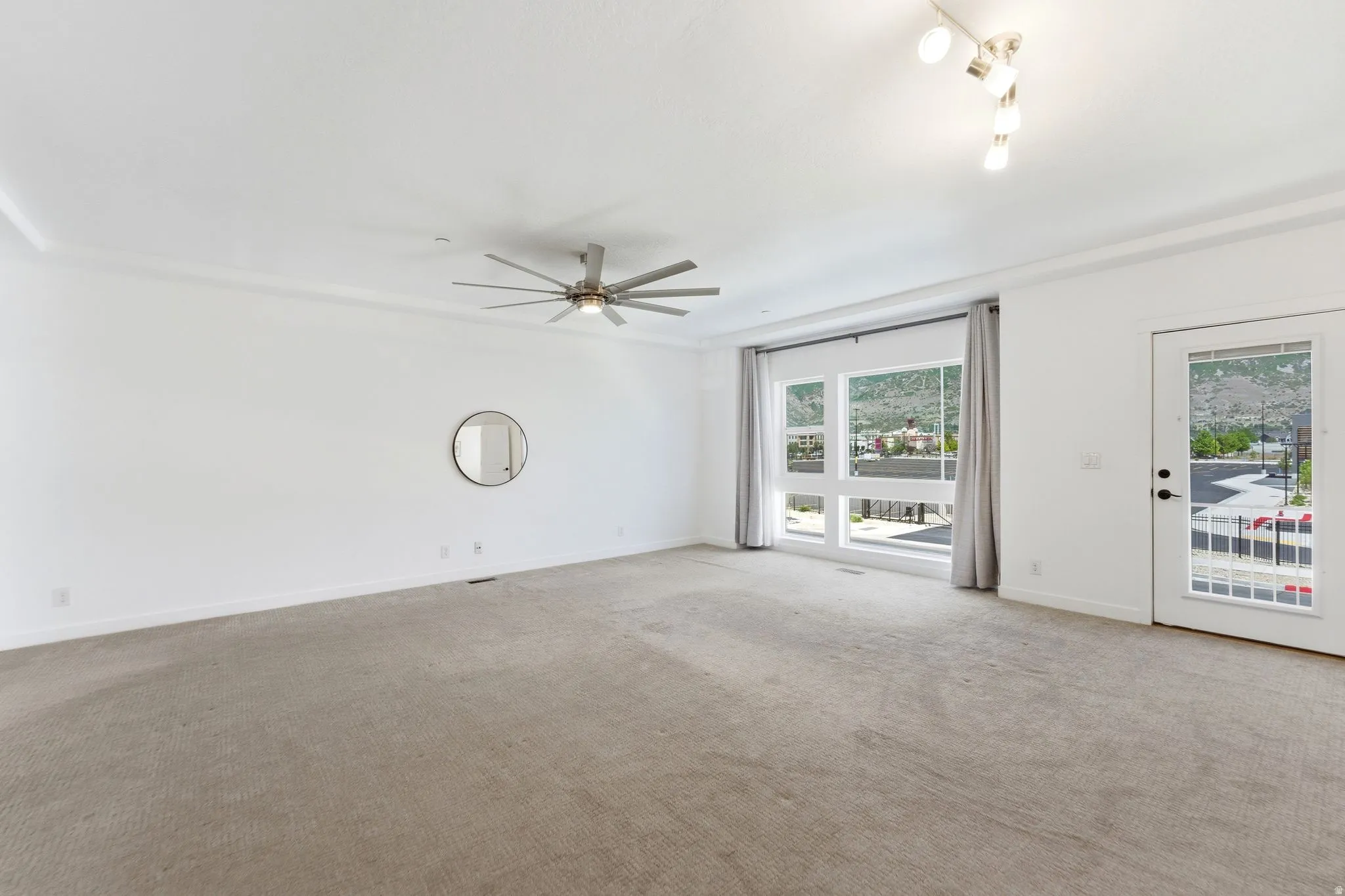 Spacious room featuring neutral carpet flooring, large multi-pane windows, a glass-panel door, contemporary ceiling fan, and decorative crown molding