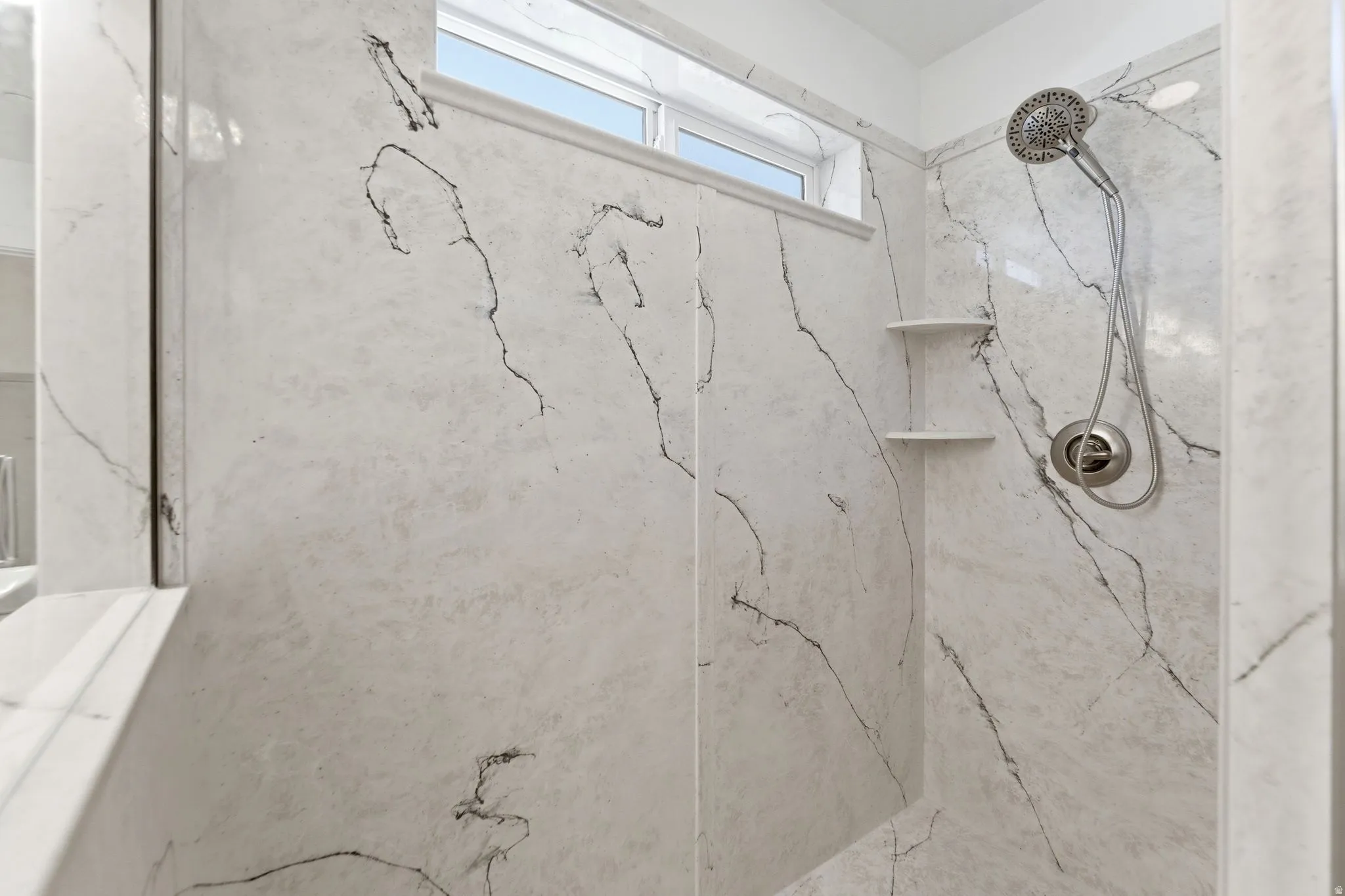Shower stall featuring large-format wall panels with black veining, a multi-function showerhead, and integrated corner shelving