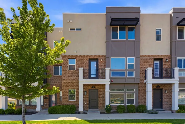 Contemporary townhome exterior featuring a brick facade, multi-pane windows, private balconies with iron railings, and a contrasting neutral color palette