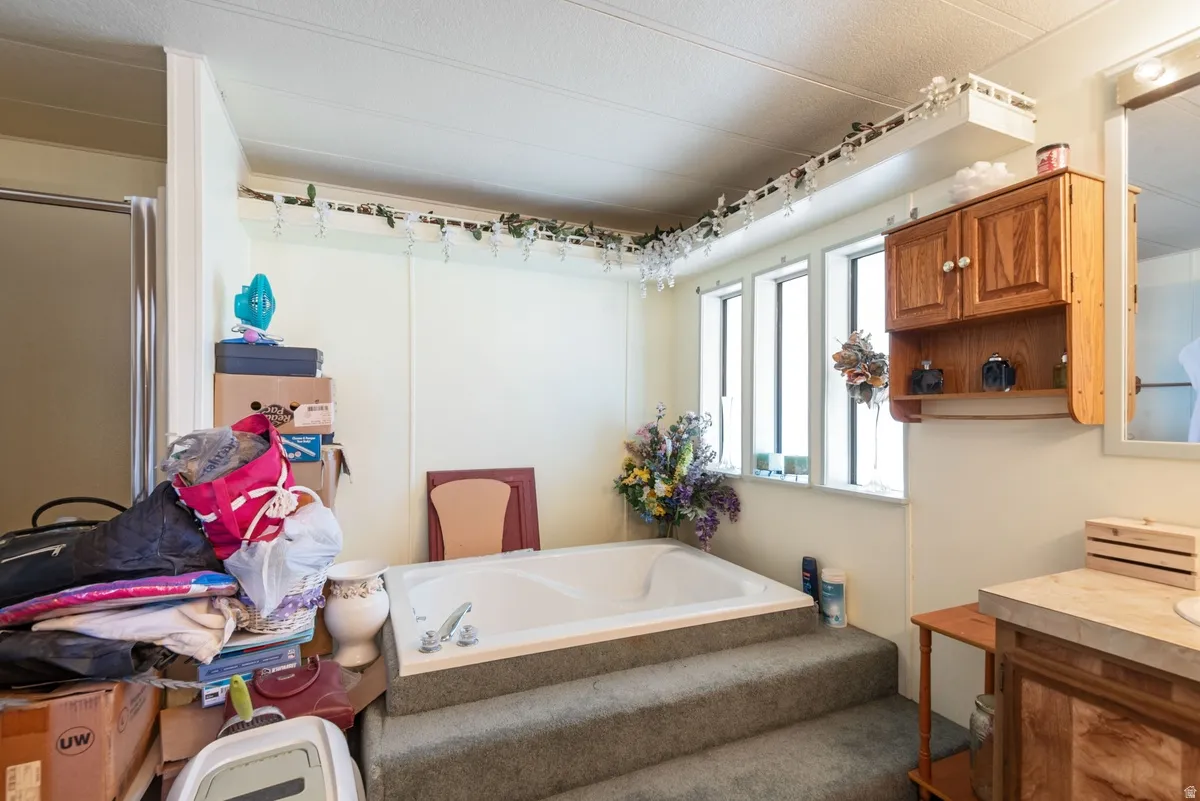 Built-in soaking tub with carpeted steps, three vertical windows, wood-finish wall cabinetry, and a vanity with a light-toned countertop
