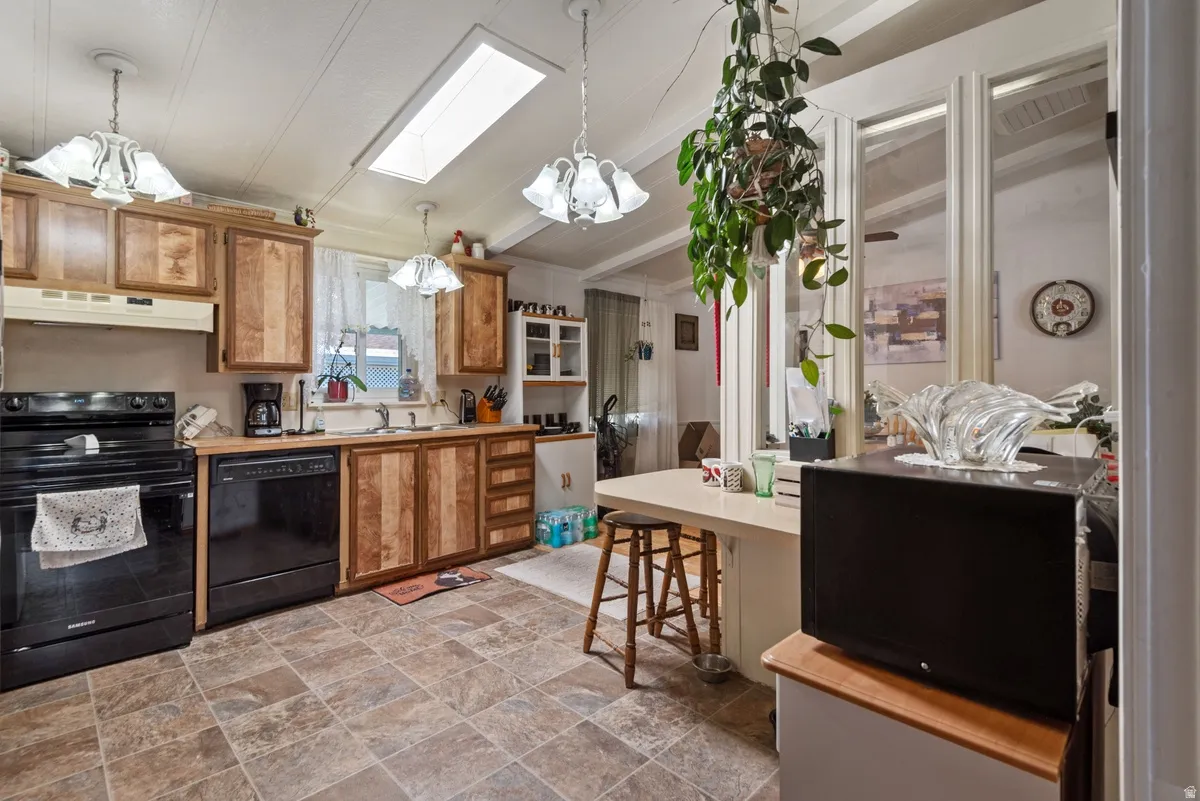 Kitchen featuring wood cabinetry, black appliances, a skylight, and durable tile flooring