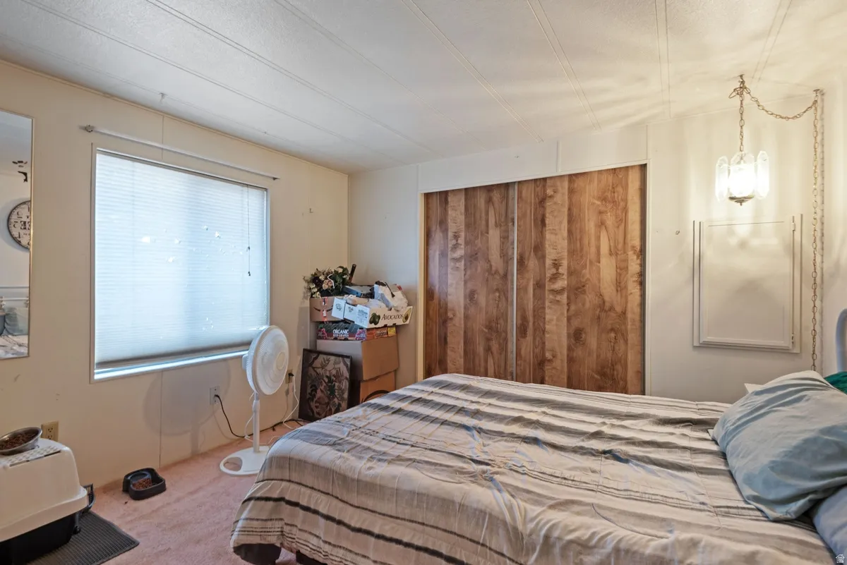 Bedroom featuring a window with blinds, wood-paneled closet doors, and a wall-mounted light fixture