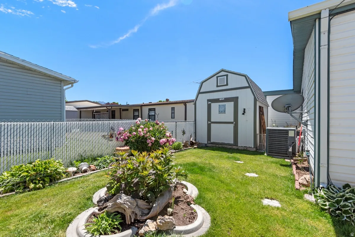 Manicured backyard featuring a chain-link fence, established landscaping, and a detached storage shed